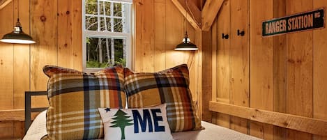 A cozy cabin room with a bed, plaid pillows, a window, and a sign reading 'RANGER STATION.'