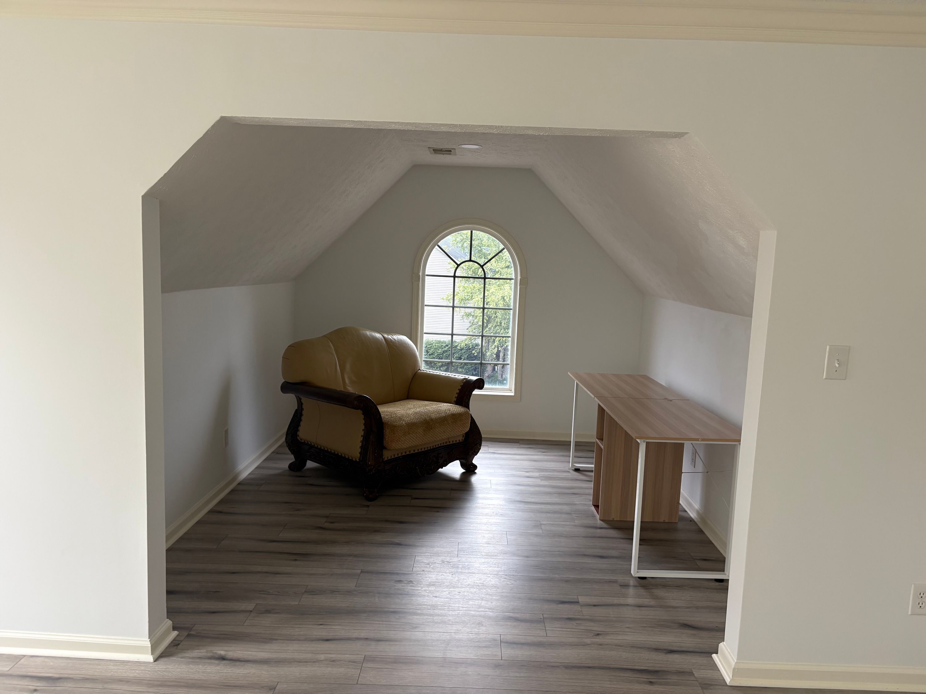 A room with a sloped ceiling, a window with a view, a chair, and a table.