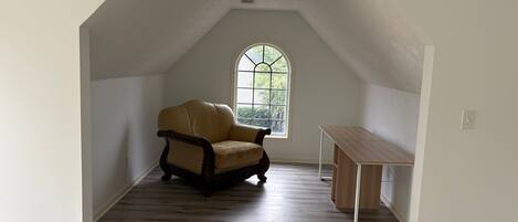 Una habitación con techo inclinado, una ventana con vistas, una silla y una mesa.