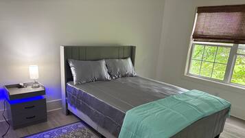 Un dormitorio con cama, mesita de noche, lámpara y ventana con persianas.