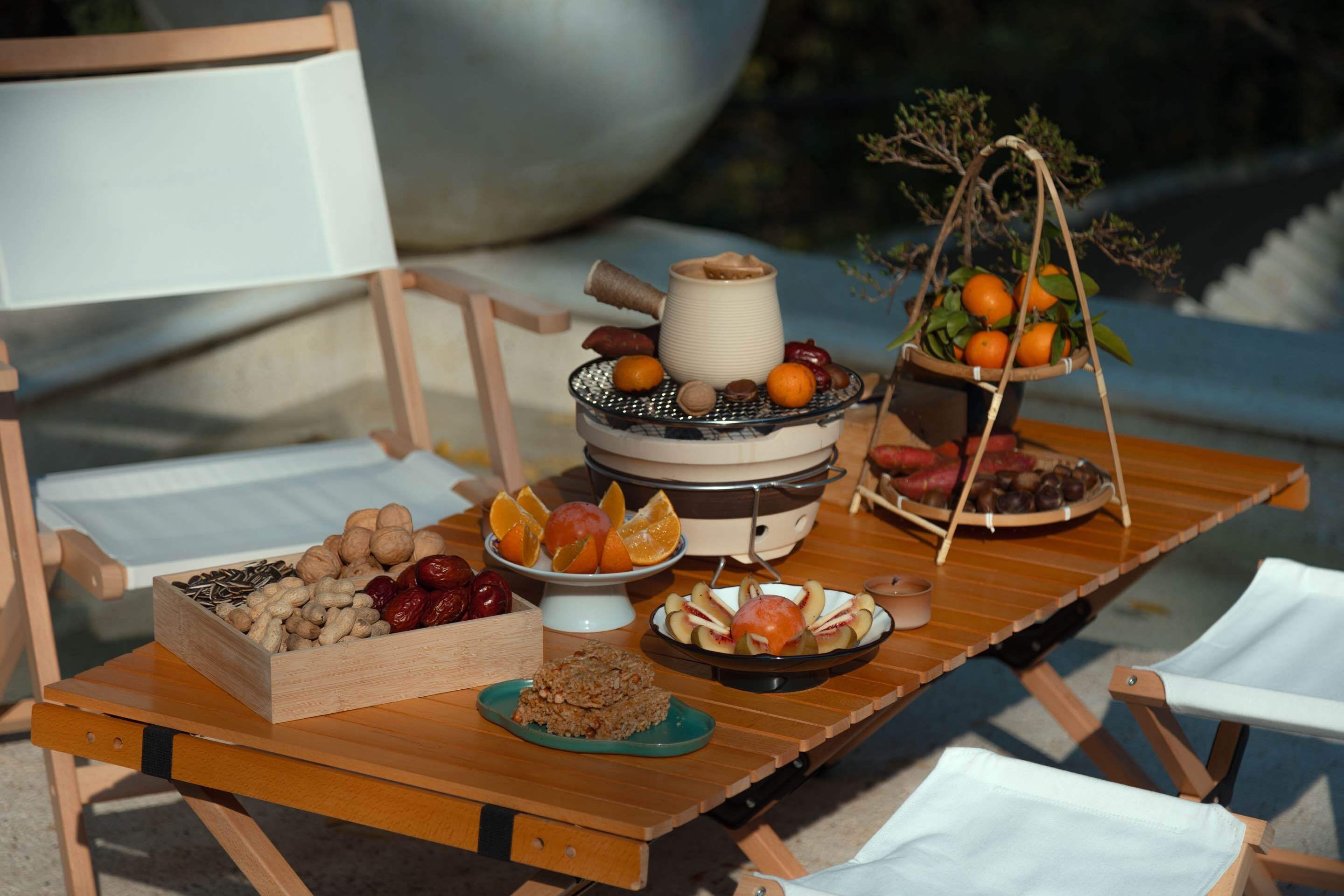 Una mesa de madera con diversas frutas y frutos secos, un tazón de galletas y una tetera.