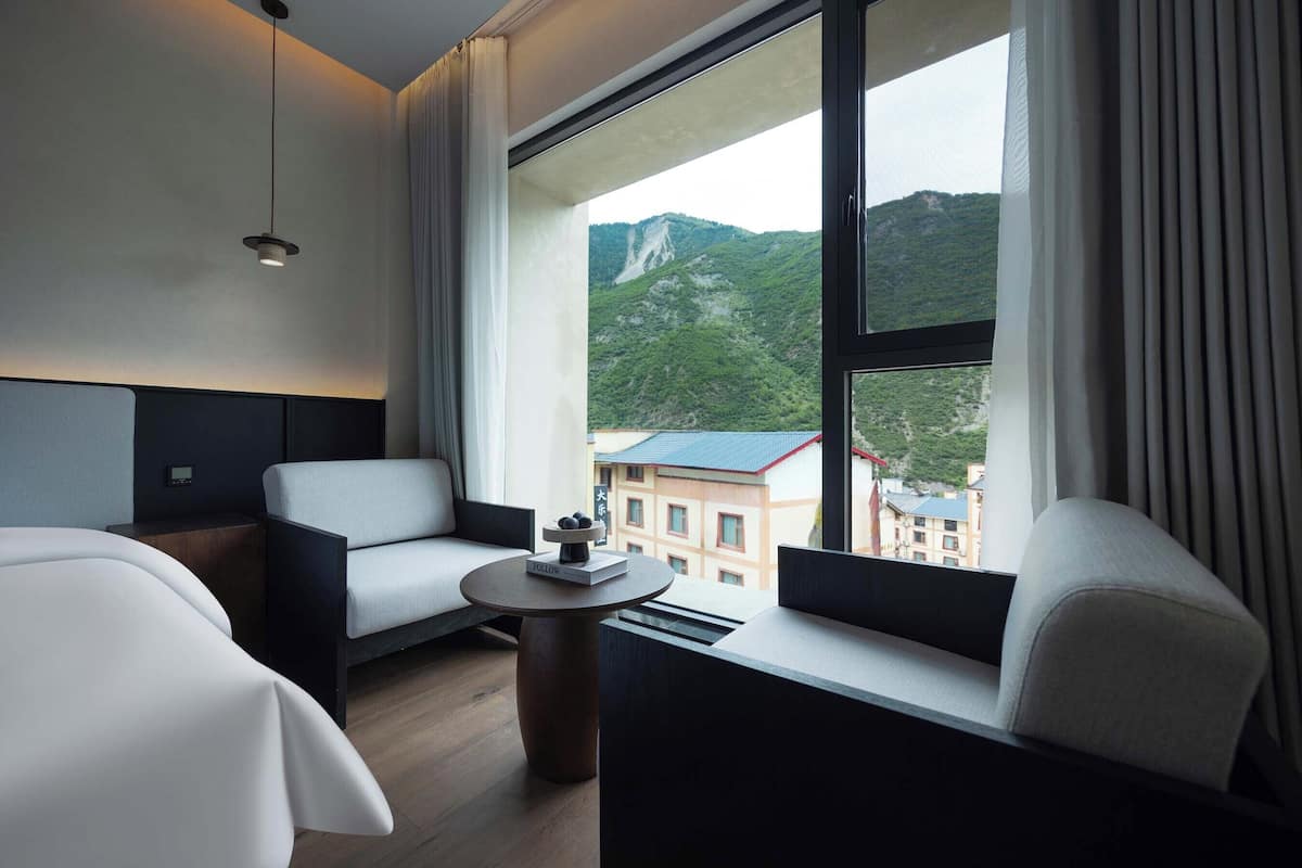A hotel room with a large window, two white sofas, a small round table with a book, and a hanging light fixture.