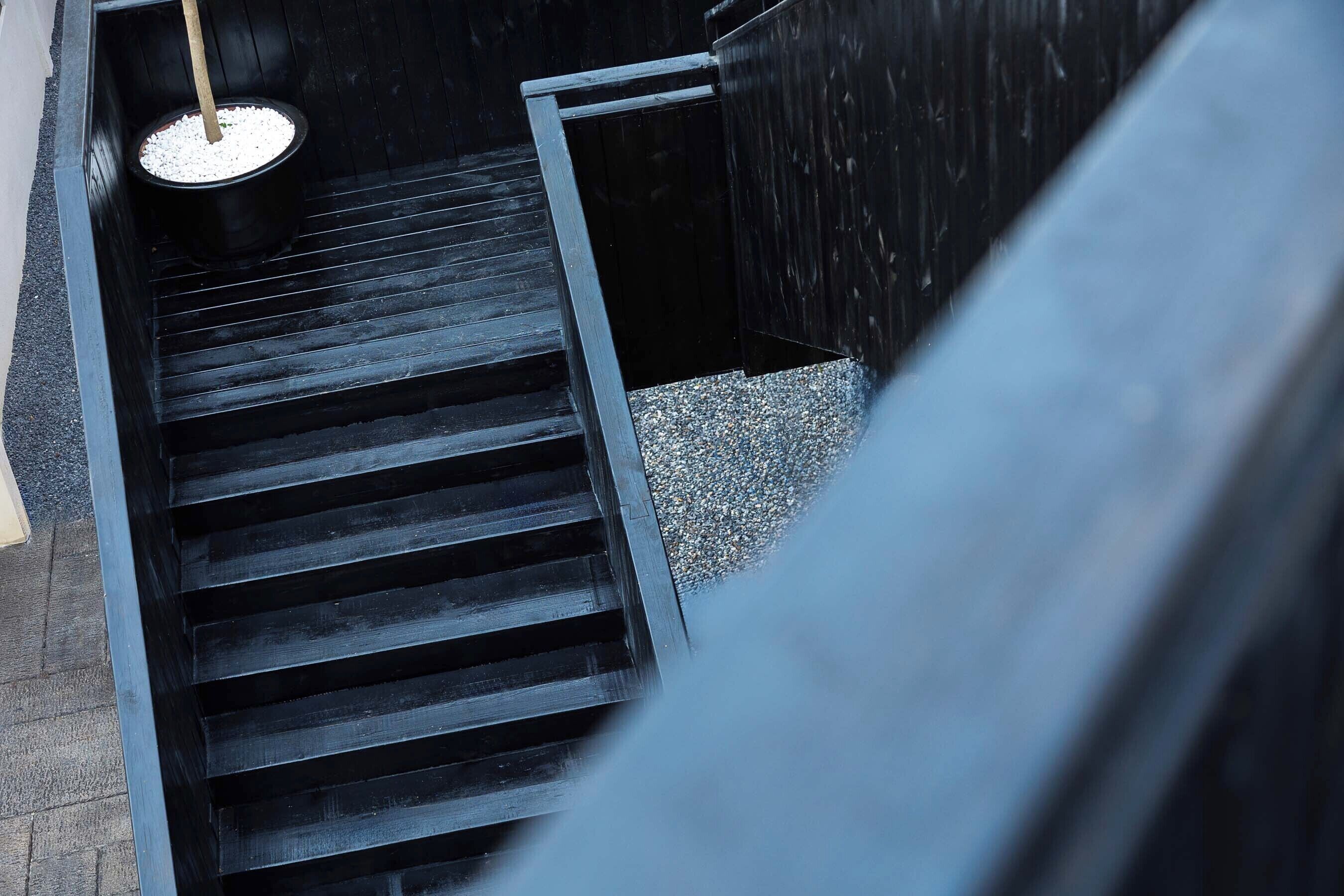 A staircase with a black railing and a pot of white pebbles at the bottom.