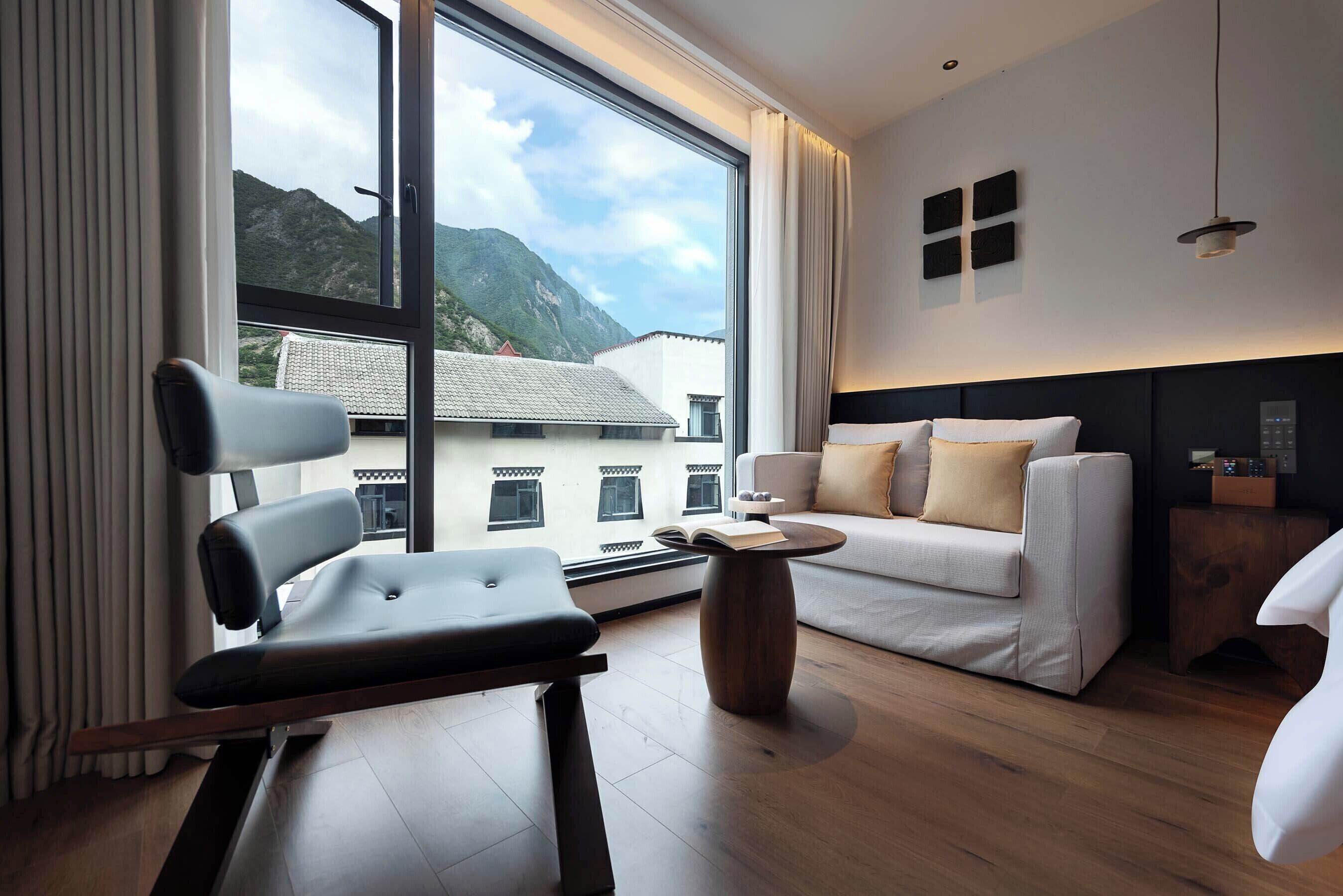 A modern hotel room with a large window, a sofa, a chair, and a small table.