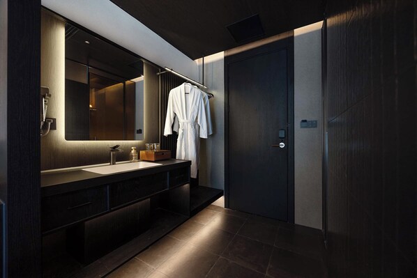A modern bathroom with a large mirror, dark wood vanity, and a robe hanging on a rack.