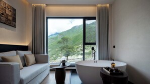 A modern bathroom with a bathtub, a sofa, and a view of a mountainous landscape. - Qinghe Courtyard Jiuzhaigou (Ngawa Autonomous Prefecture)