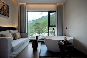 Un baño moderno con bañera, sofá y vistas a un paisaje montañoso.