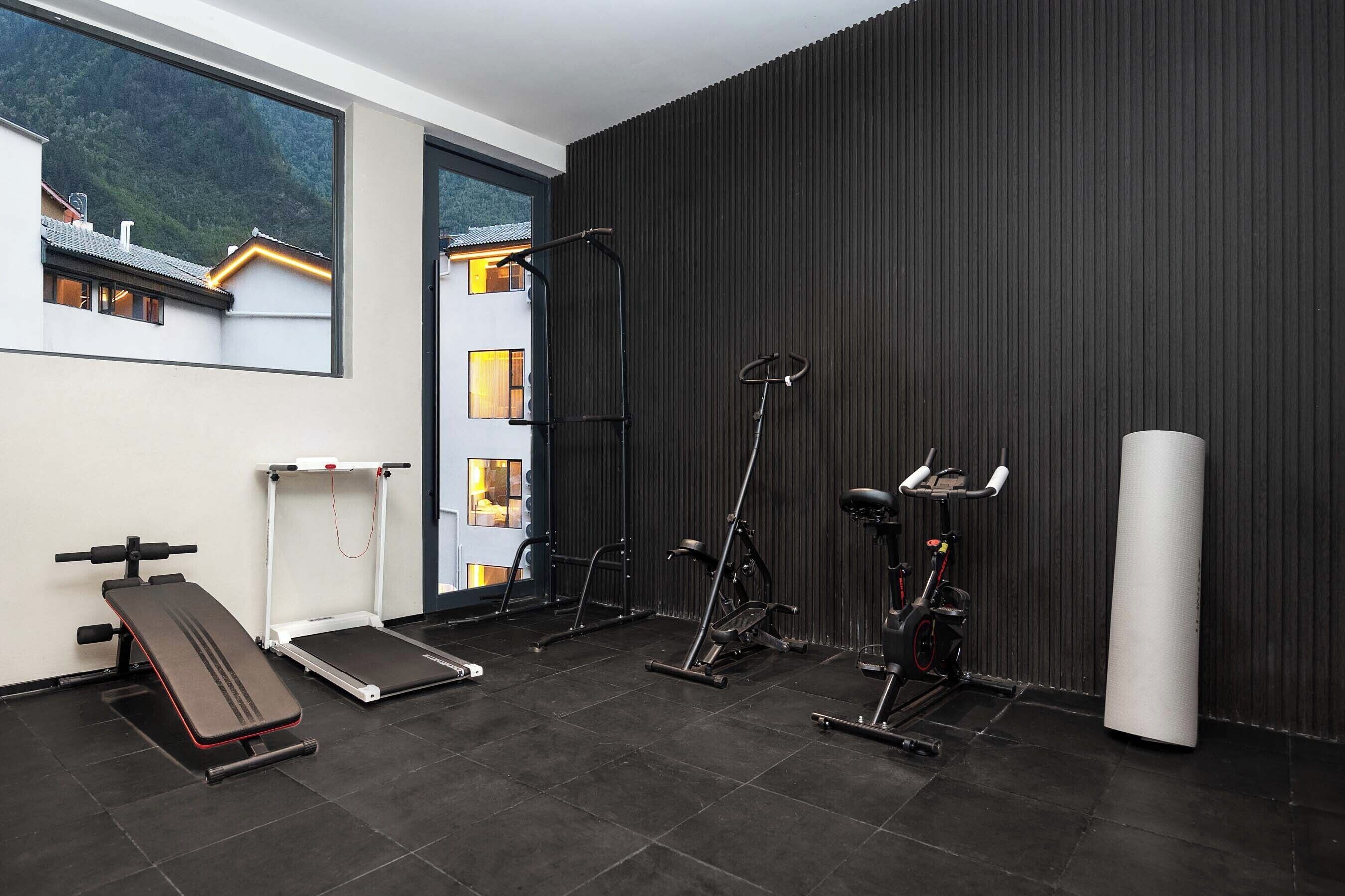 A gym with a bench, elliptical, and exercise bike, a large window, and a view of buildings.