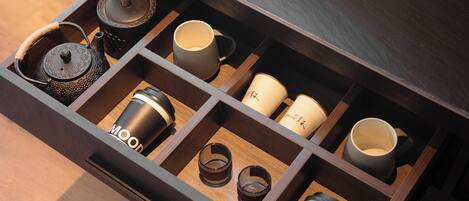 A drawer with compartments containing a teapot, cups, and a coffee grinder.