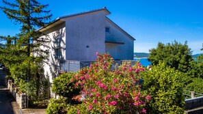 Ein zweistöckiges Gebäude mit Balkon, umgeben von üppigem Grün und Blick aufs Meer.