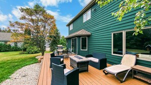 A deck with outdoor furniture, a house with green siding, and a tree with autumn leaves. - Luxurious Retreat with Expansive Yard in Sister Bay, Wisconsin (Sister Bay)