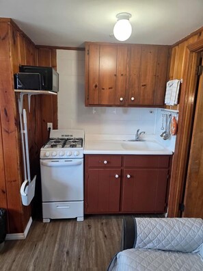 A compact kitchen with wooden cabinets, a white stove, and a sink. - Unwind Steps from the Ocean in Coastal Serenity in North Truro, Massachusetts (North Truro)