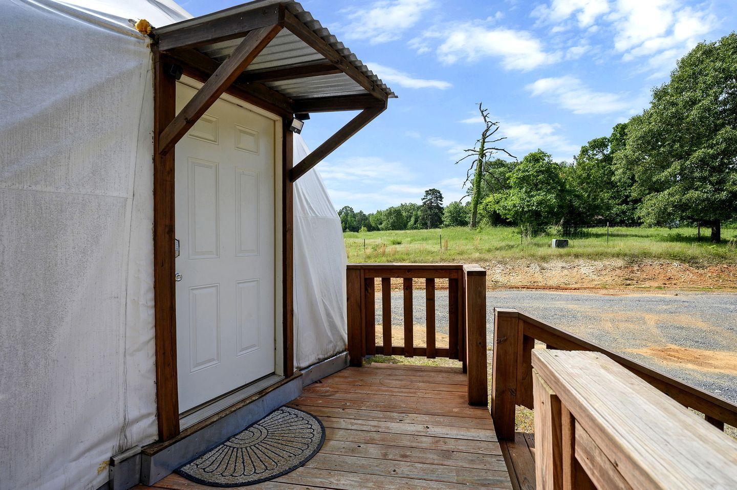 Une véranda couverte avec une balustrade en bois, une porte et une vue sur un paysage rural.