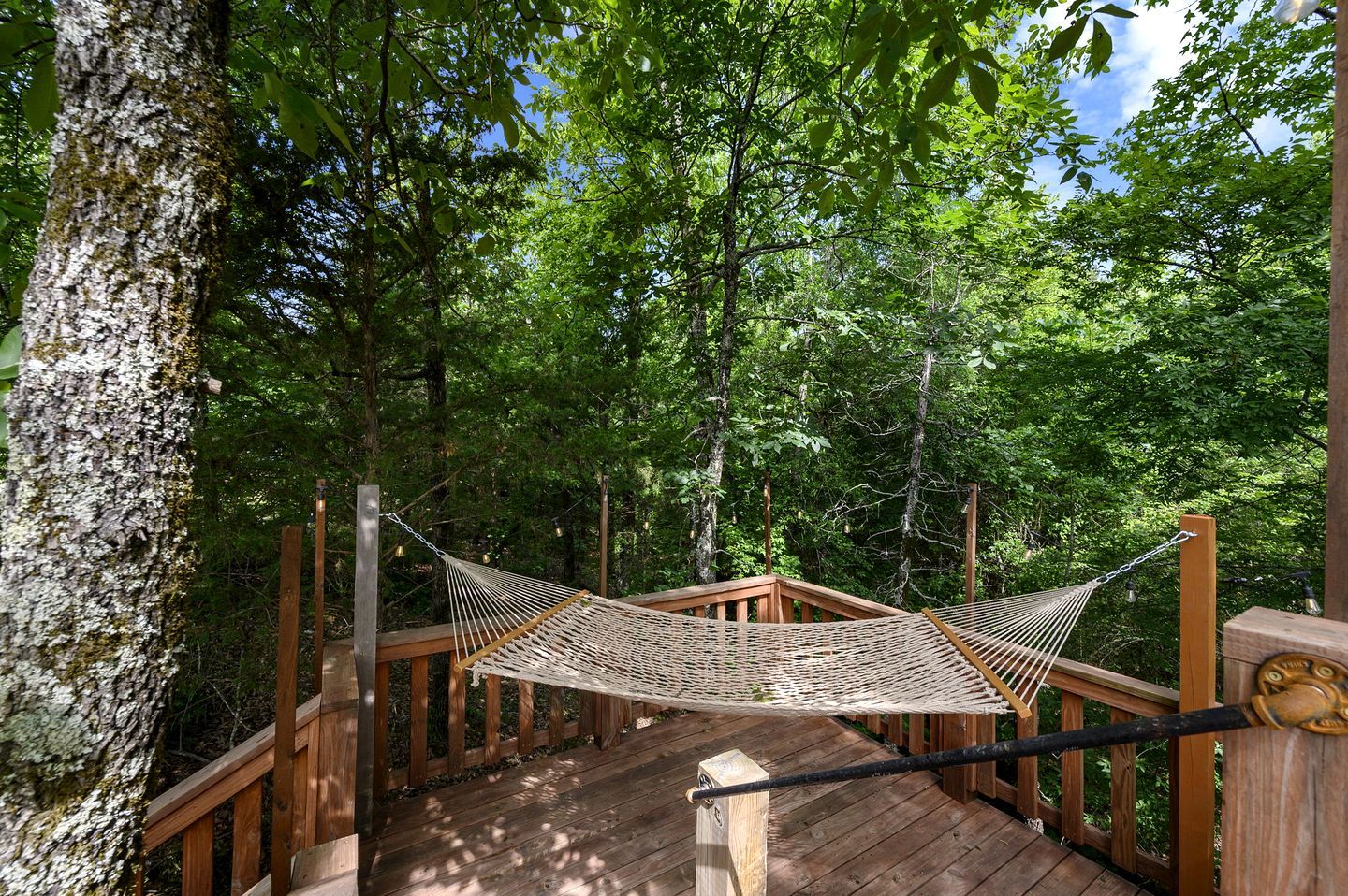 A hammock suspended between wooden beams on a wooden deck surrounded by trees.