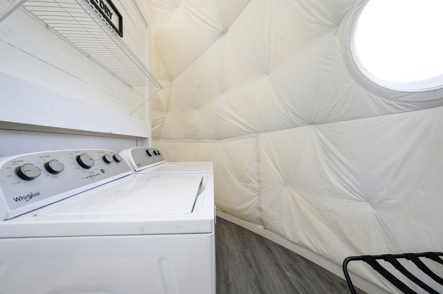 A laundry room with a Whirlpool washer and dryer, a metal shelf, and a window.