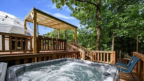 A hot tub with a wooden deck, a covered seating area, and a hammock.