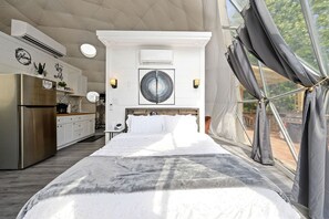 Quarto moderno com cama grande, cozinha e vista pela janela com cortinas.