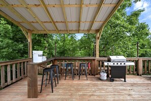 Eine Terrass mit Grill, Barhocker und einem weißen Behälter mit der Aufschrift 'YARD'.