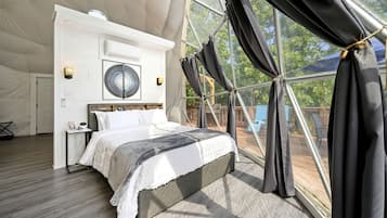 A spacious bedroom with a large bed, a ceiling fan, and a view through a large window with curtains.