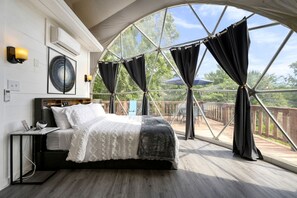 A bedroom with a large window, a bed, a bedside table, and a wall-mounted fan.