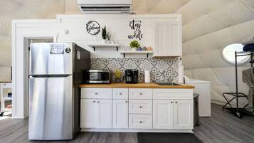 A compact kitchen with a stainless steel refrigerator, a microwave, and a coffee maker on the countertop.