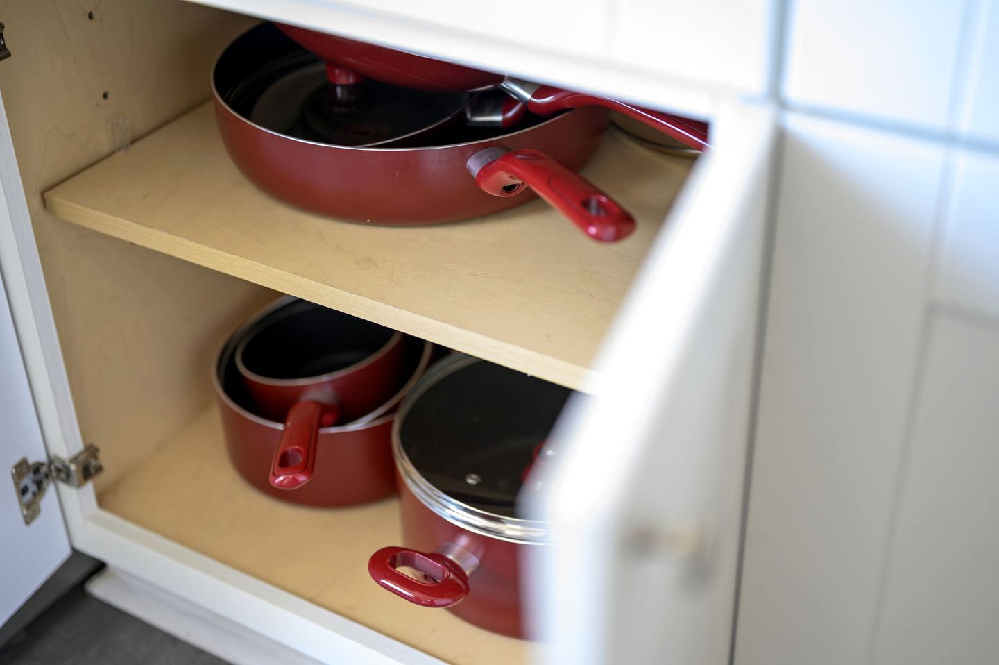 Un armario de cocina con dos estantes, cada uno con utensilios de cocina rojos.