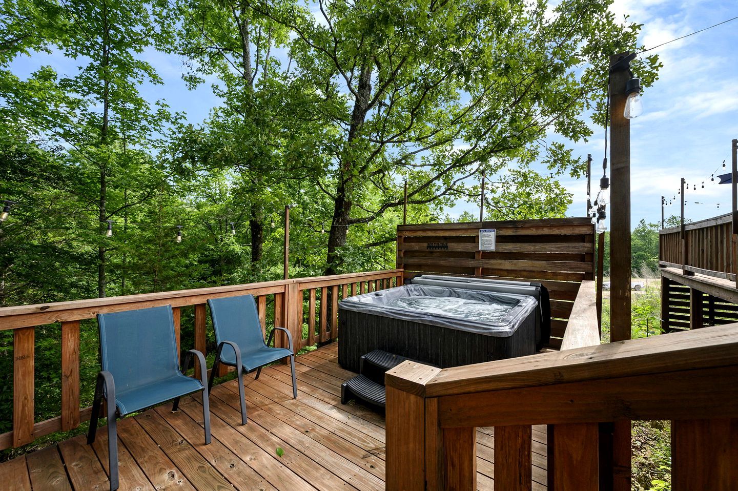 A wooden deck with a hot tub, two blue chairs, and a wooden railing.