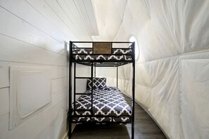 Een stapelbed met beddengoed met patroon in een smalle kamer met witte muren en een houten vloer.