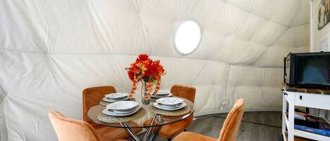 A dining area with a round glass table, orange chairs, and a white tent-like structure in the background.