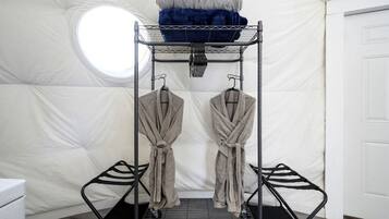 A bunk bed with a circular window, two robes hanging on hooks, and a white door.