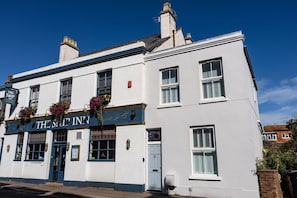 A white building with a sign reading 'The Ship Inn' and flower boxes above the entrance.