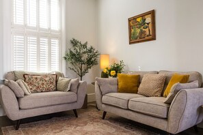 A living room with two sofas, a floor lamp, a potted plant, and a painting on the wall.