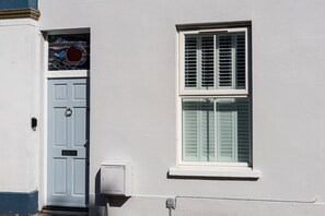 Eine Gebäudefassade mit einer weißen Tür, einem Fenster mit Rollläden und einem kleinen Verteilerkasten.