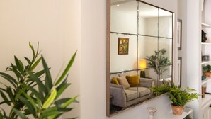 A room with a large mirror reflecting a sofa and a lamp. There is a plant on a shelf and a white vase on the floor. - Little Meads House - charming cottage close to seafront (Eastbourne)