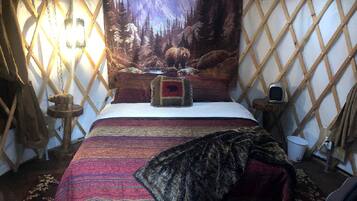 A yurt interior with a bed, a tapestry, and a wooden table.
