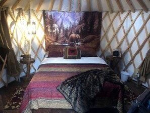 L’intérieur d’une yourte, avec un lit, une tapisserie et une table en bois.
