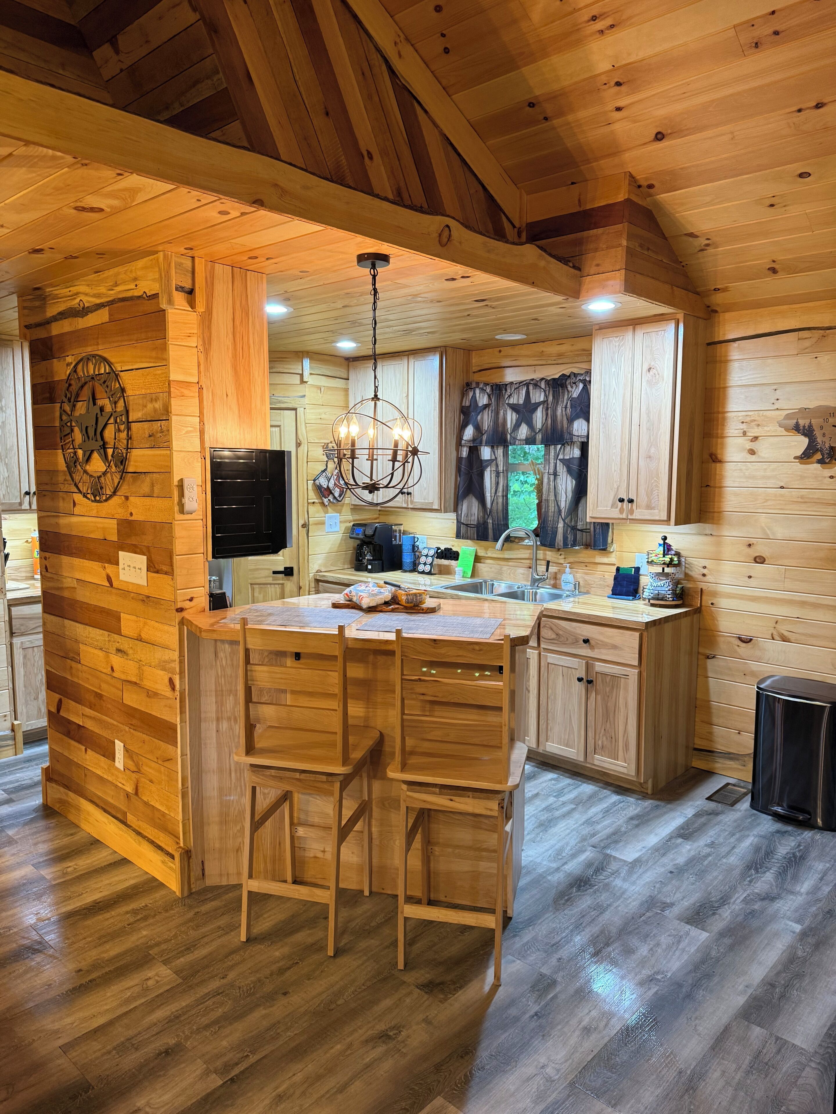 L’intérieur d’un chalet en bois comprend un îlot de cuisine, des tabourets de bar, un lustre et une horloge murale.