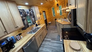 L’intérieur d’un chalet en bois comprend un coin cuisine, des placards en bois, une machine à café et un évier.