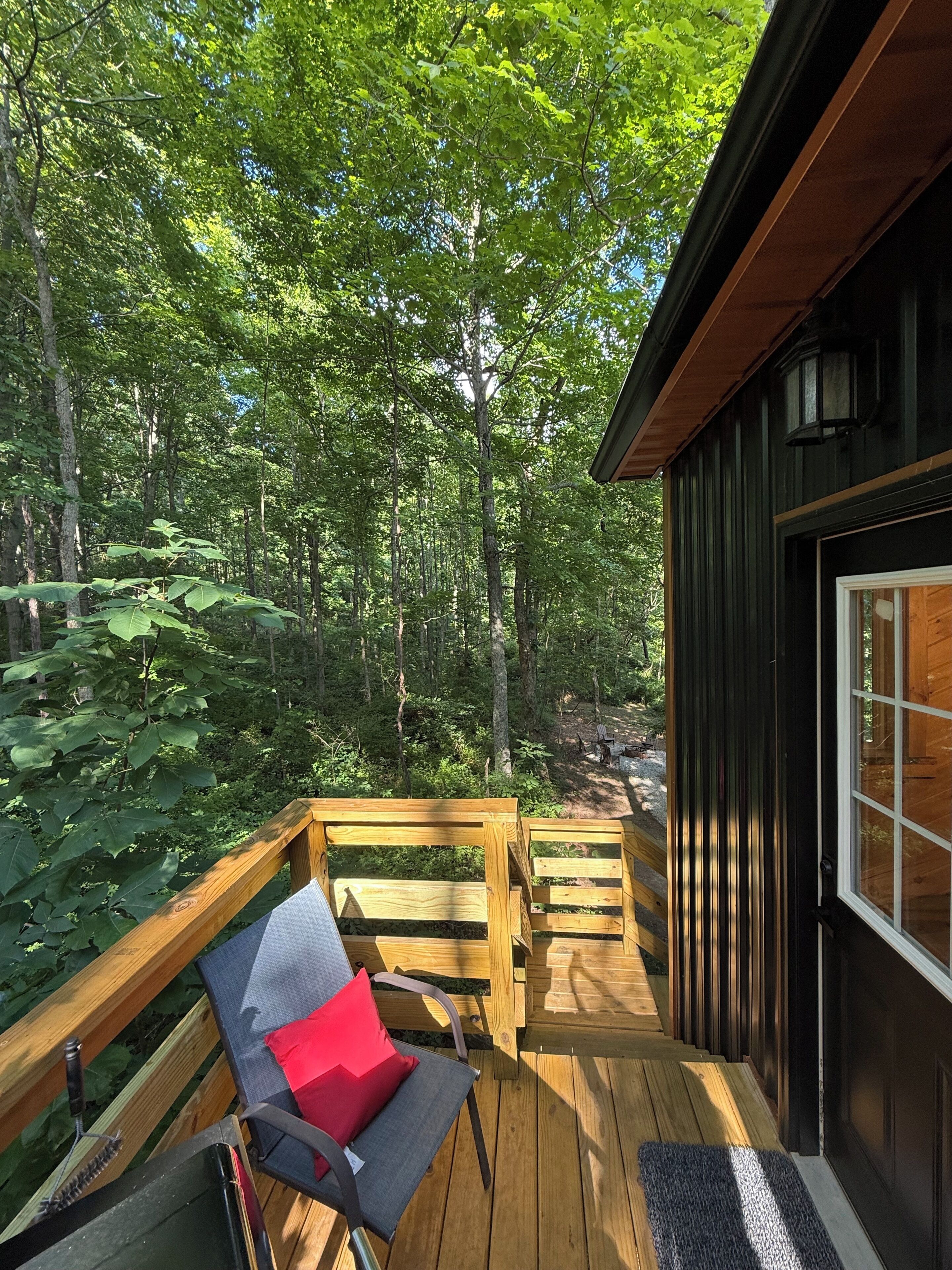 Une terrasse en bois avec une chaise et un coussin rouge, entourée d’une forêt.