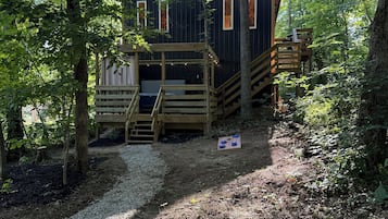 Une cabane dotée d’une terrasse en bois, d’un escalier et d’un petit espace extérieur aménagé pour s’asseoir.
