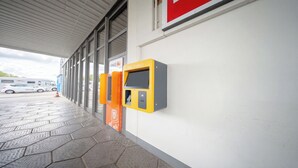 Un quiosco de auto-registro en la entrada de un edificio, con suelo de baldosas y un pasillo cubierto.