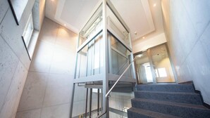 Un interior moderno con un ascensor de vidrio, pisos de mármol y una escalera.