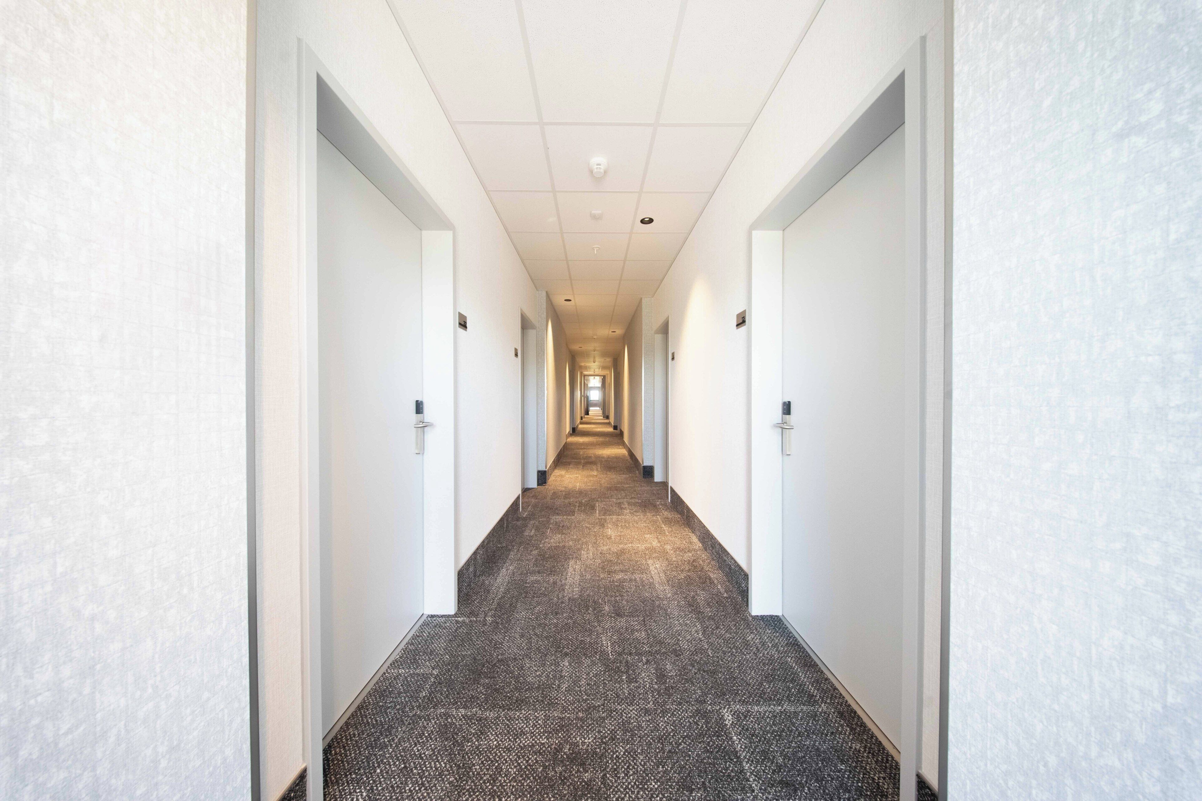 Un largo pasillo de hotel, con piso alfombrado y paredes blancas.