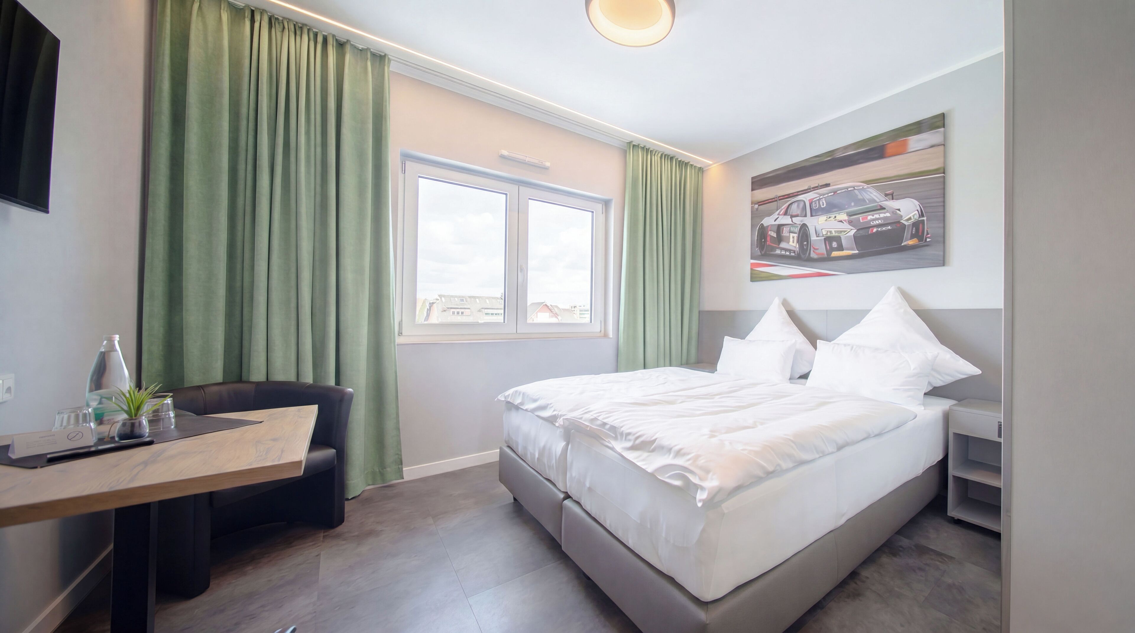A hotel room with a bed, a desk, a chair, a window, and a painting on the wall.