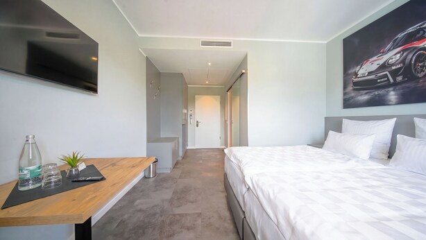 Una habitación de hotel con una cama, un escritorio con una planta, un televisor y un cartel en la pared.