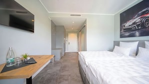 Una habitación de hotel con una cama, un escritorio con una planta, un televisor y un cartel en la pared.