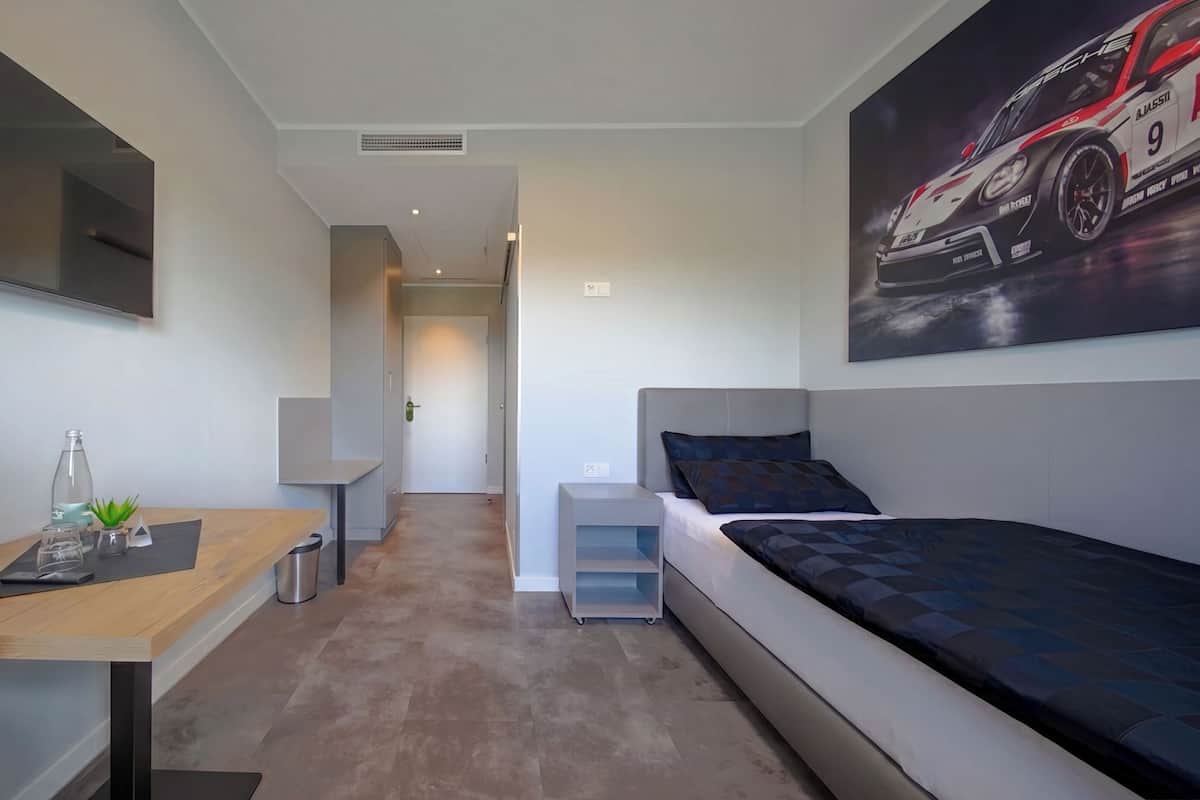Ein modernes Schlafzimmer mit einem Bett, einem Schreibtisch, einem Sessel, einem kleinen Tisch mit Pflanze und einem an der Wand montierten Fernseher.