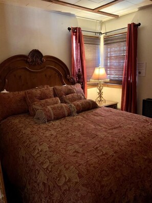 Ein Schlafzimmer mit einem großen Bett, einem Nachttisch mit Lampe und einem Fenster mit Vorhängen.