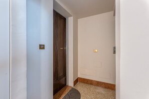 Passadís estret amb una porta, un interruptor de llum i una paret amb una làmpada.