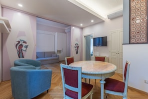 Een eetgedeelte met een ronde tafel en stoelen, een bank en een televisie aan de muur.